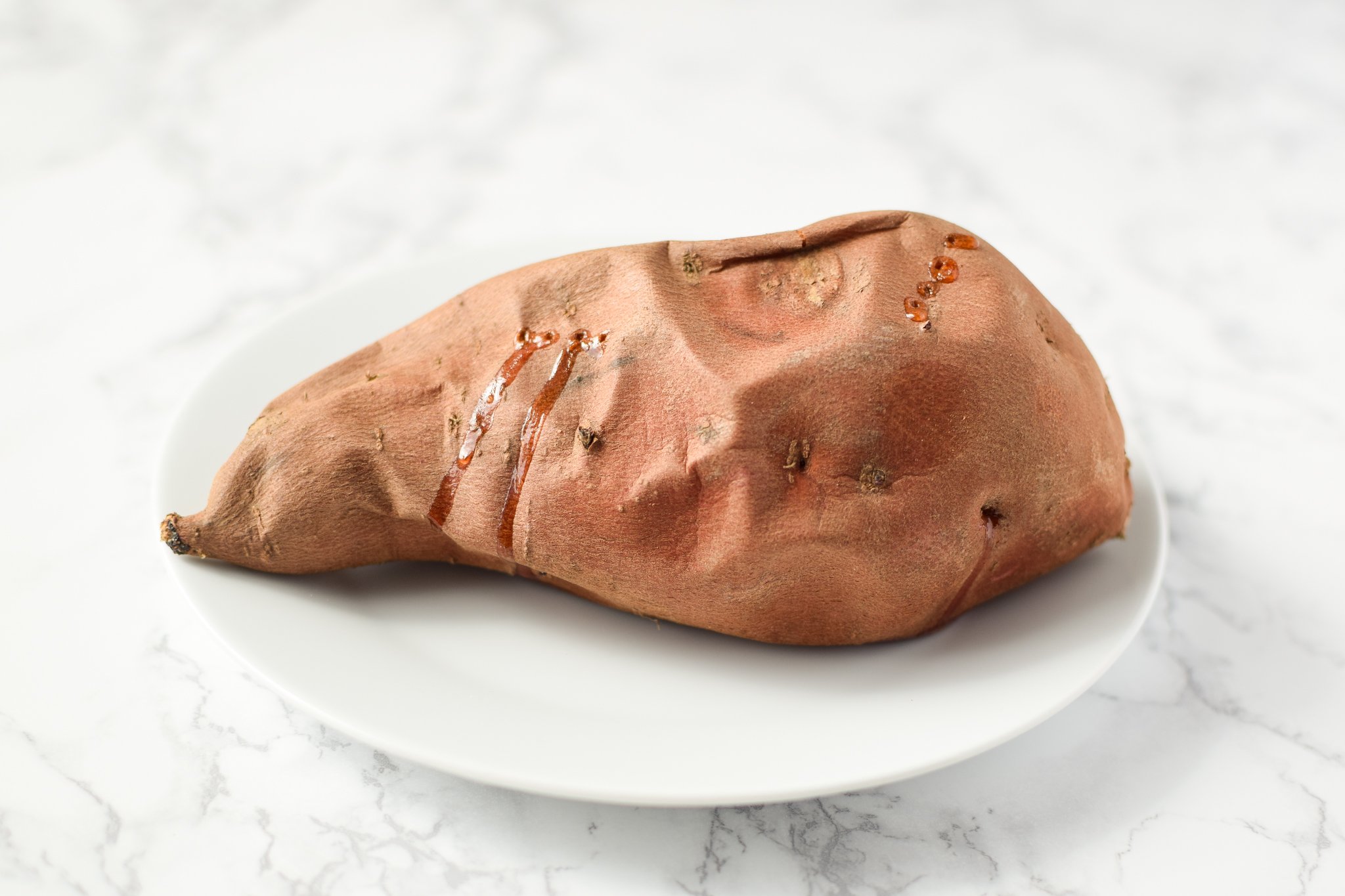 A baked sweet potato cooling on a white plate.