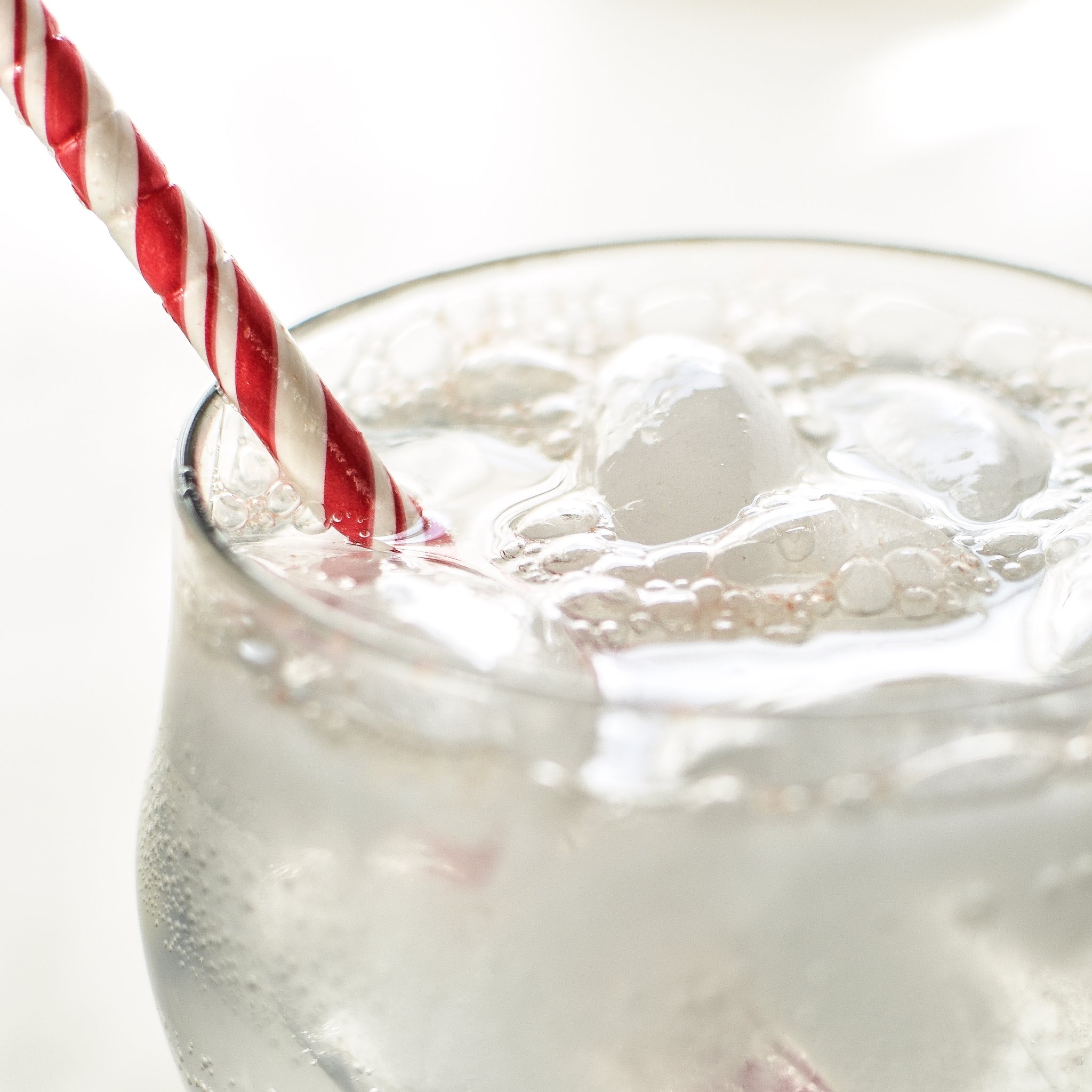 A cold fizzy beverage with lots of bubbles at the top and a red and white candy cane striped straw. Homemade LaCroix