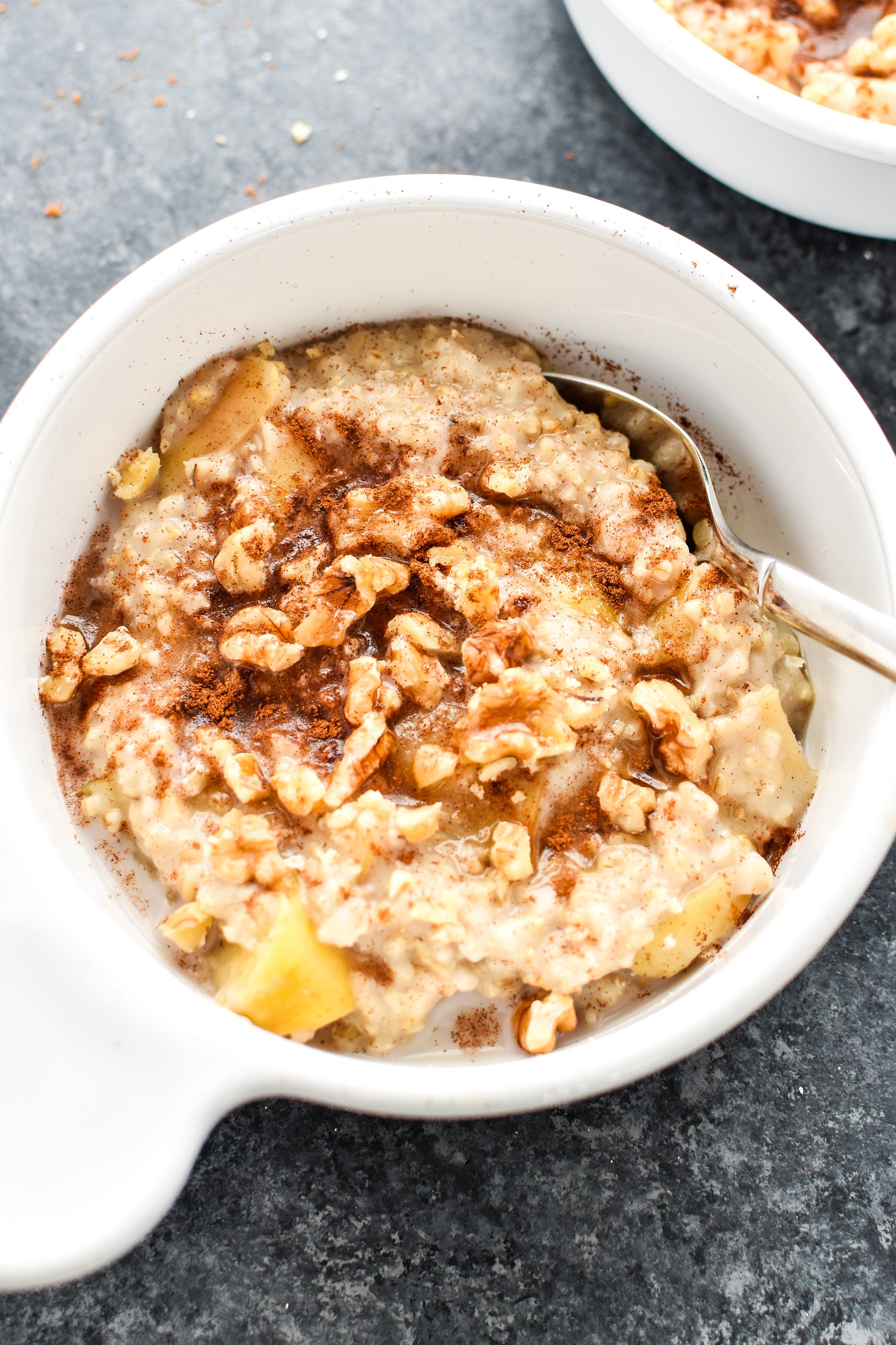 A bowl of cooked oatmeal with apples, cinnamon and walnuts.