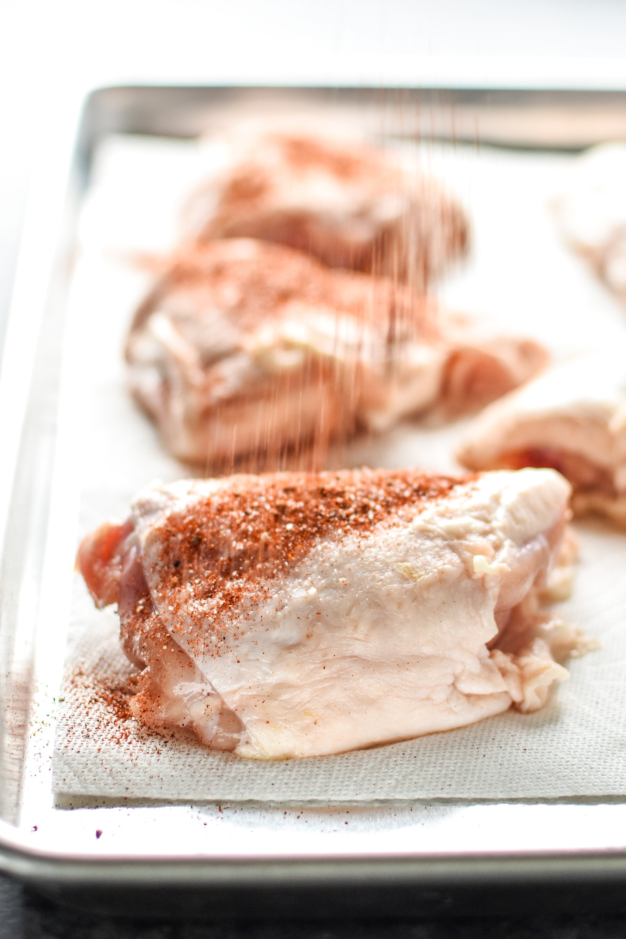 Sprinkles spices onto raw bone in chicken thighs.