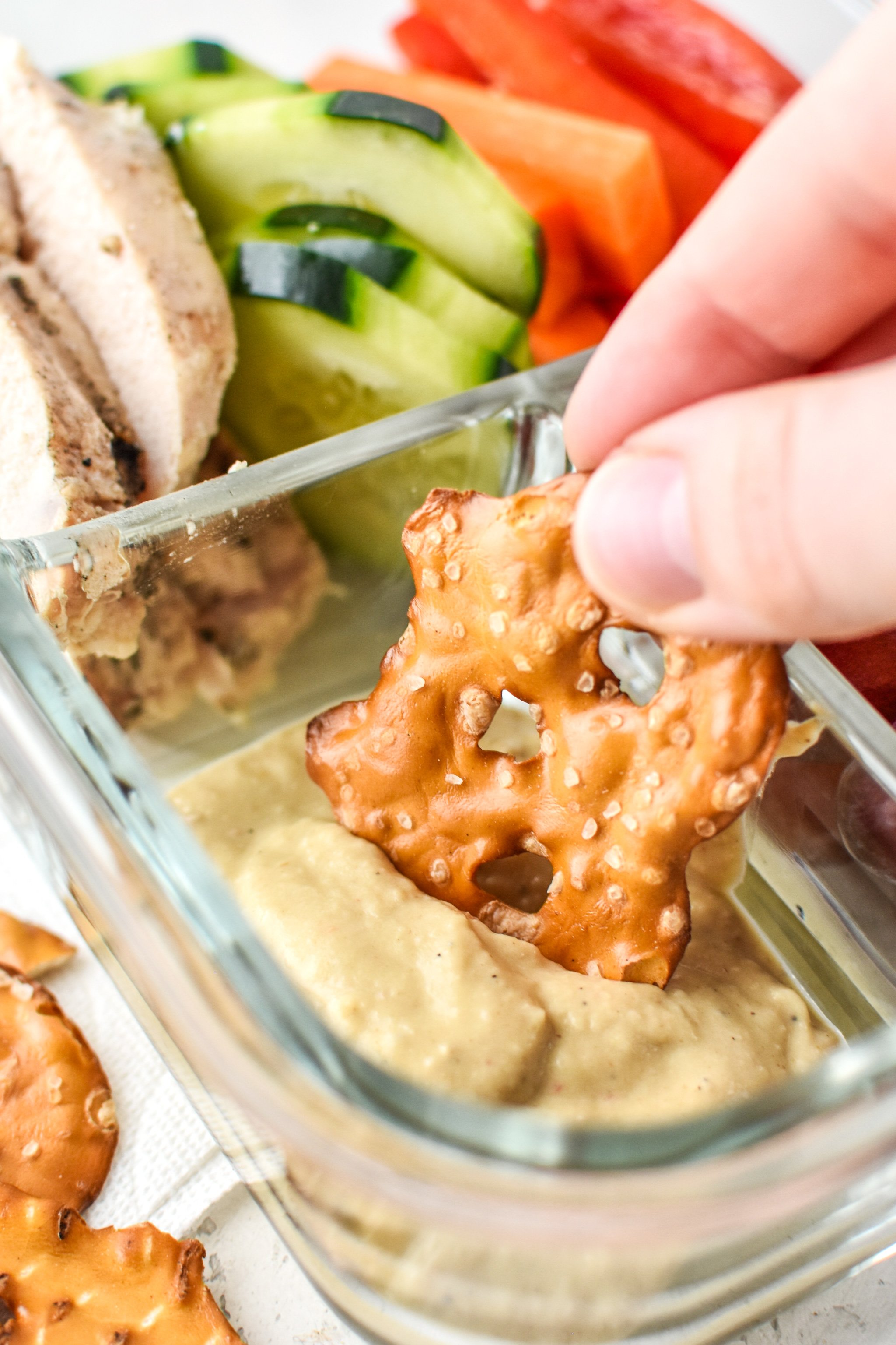 Dipping a pretzel into the hummus of the Chicken & Hummus Plate Lunch Meal Prep.