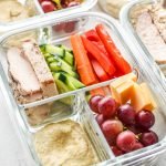A glass container with chicken, pepper, carrots, cucumber, and more meal prepped for lunch.