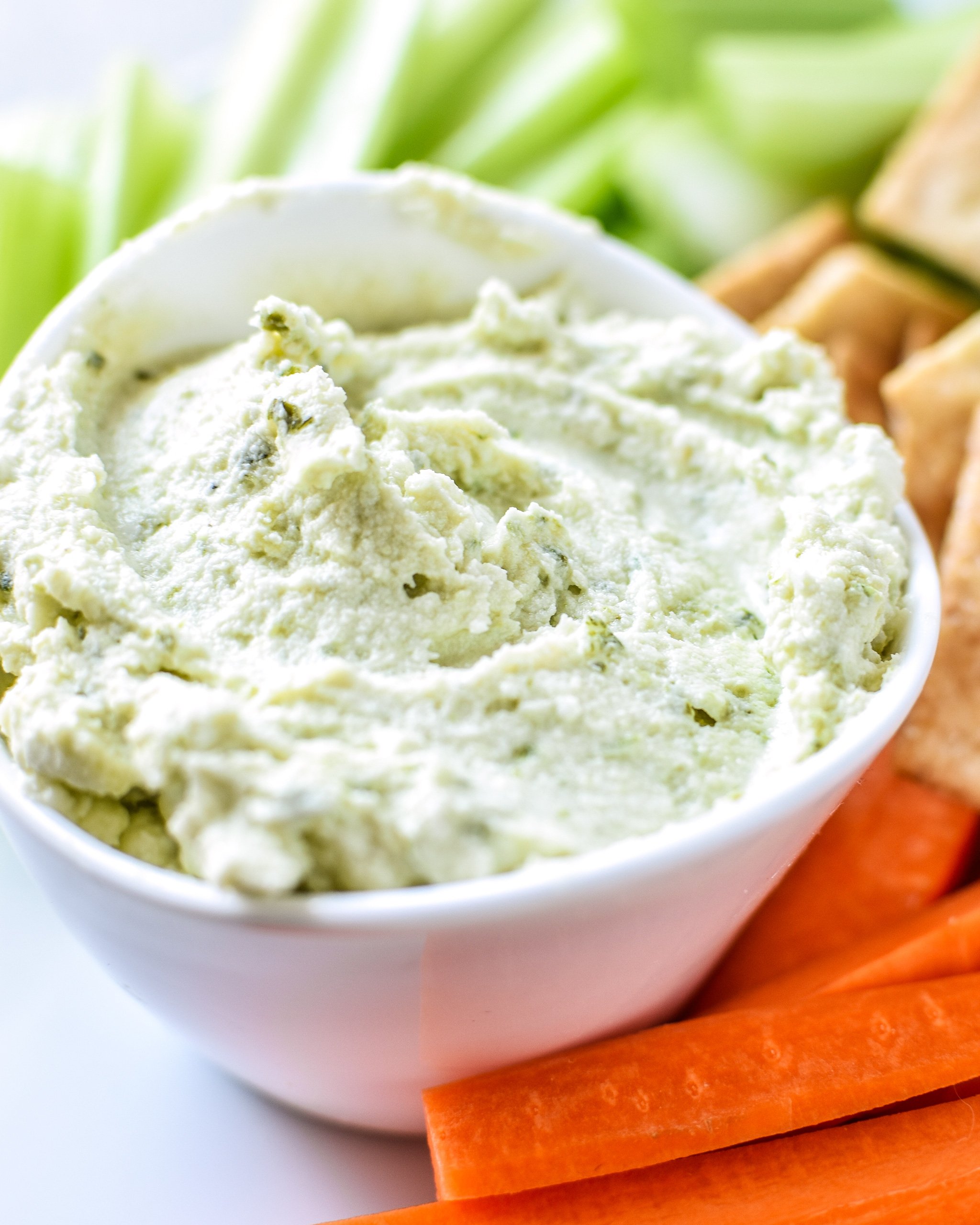 A cup of 3-Ingredient Pesto Goat Cheese Dip with carrots, celery and crackers.