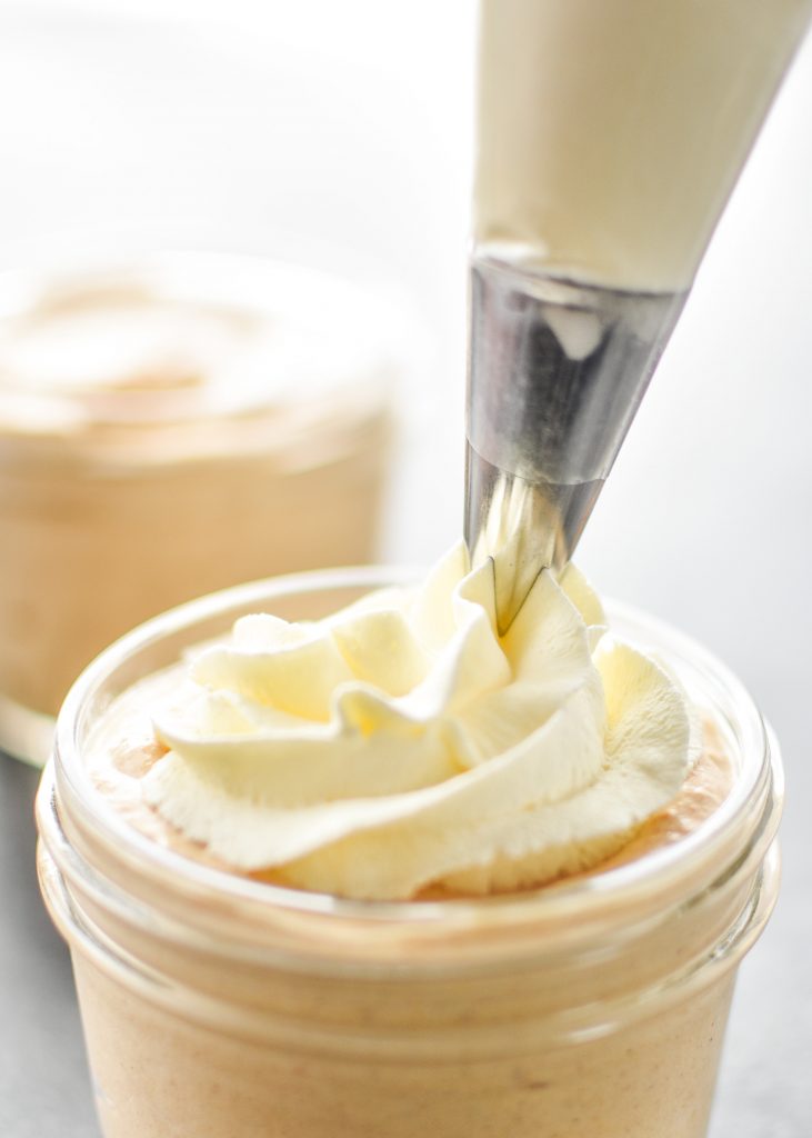 piping whipped cream onto pumpkin spice greek yogurt.