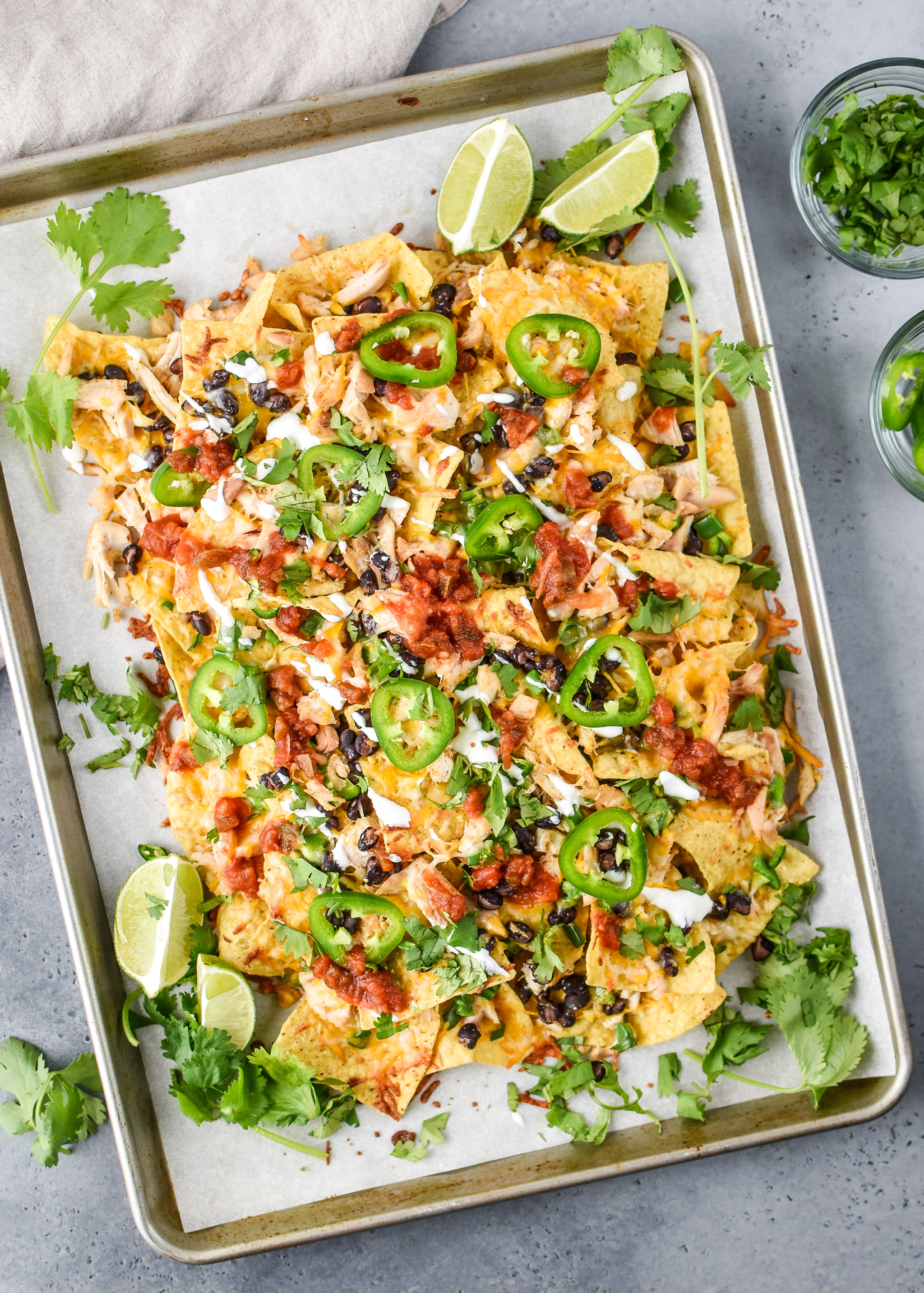 A pan of beautiful Prep Ahead Rotisserie Chicken Nachos covered in cilantro, sour cream and salsa.