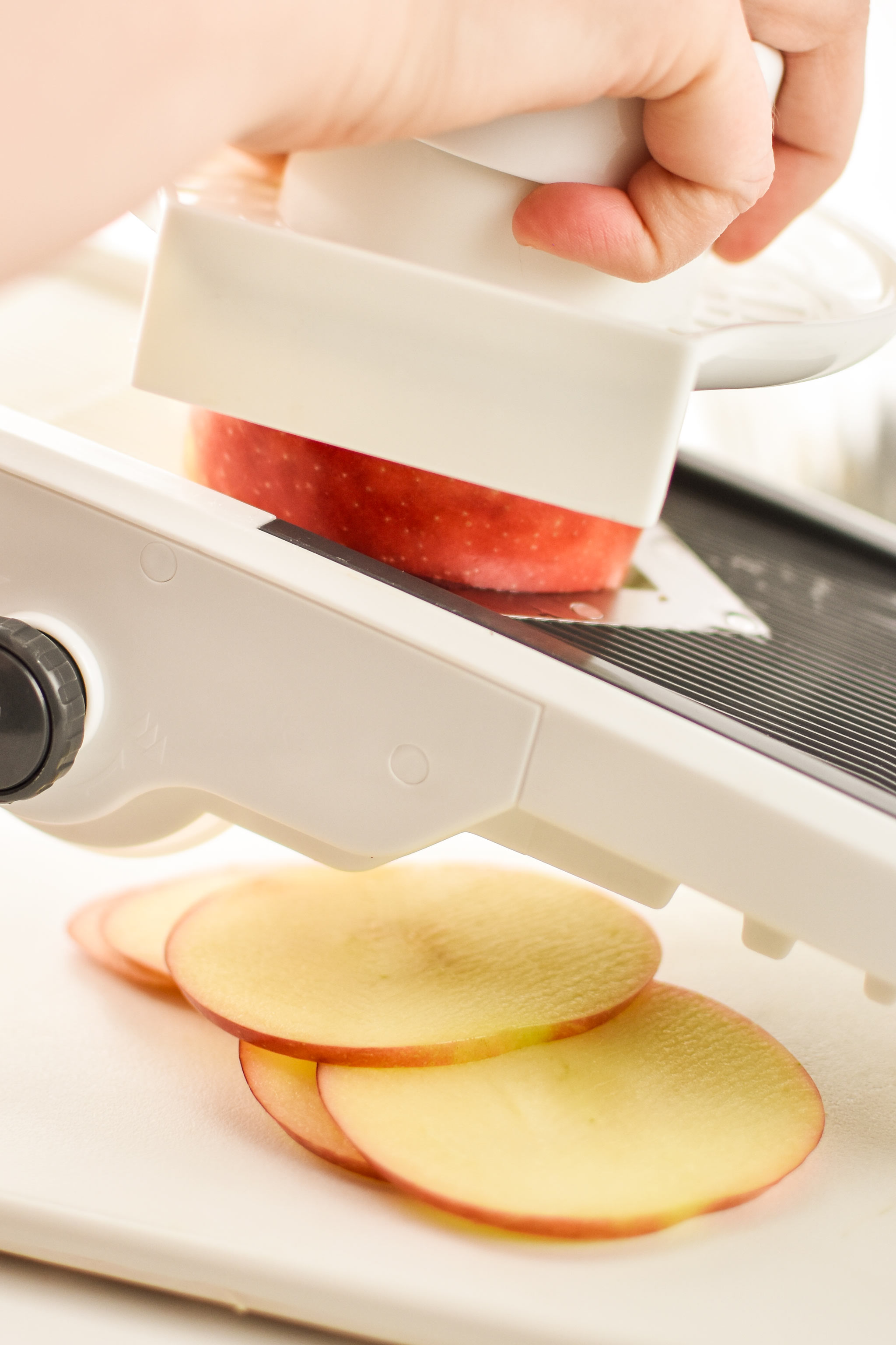 An apple being cut with a mandoline to make apple chips in an air fryer