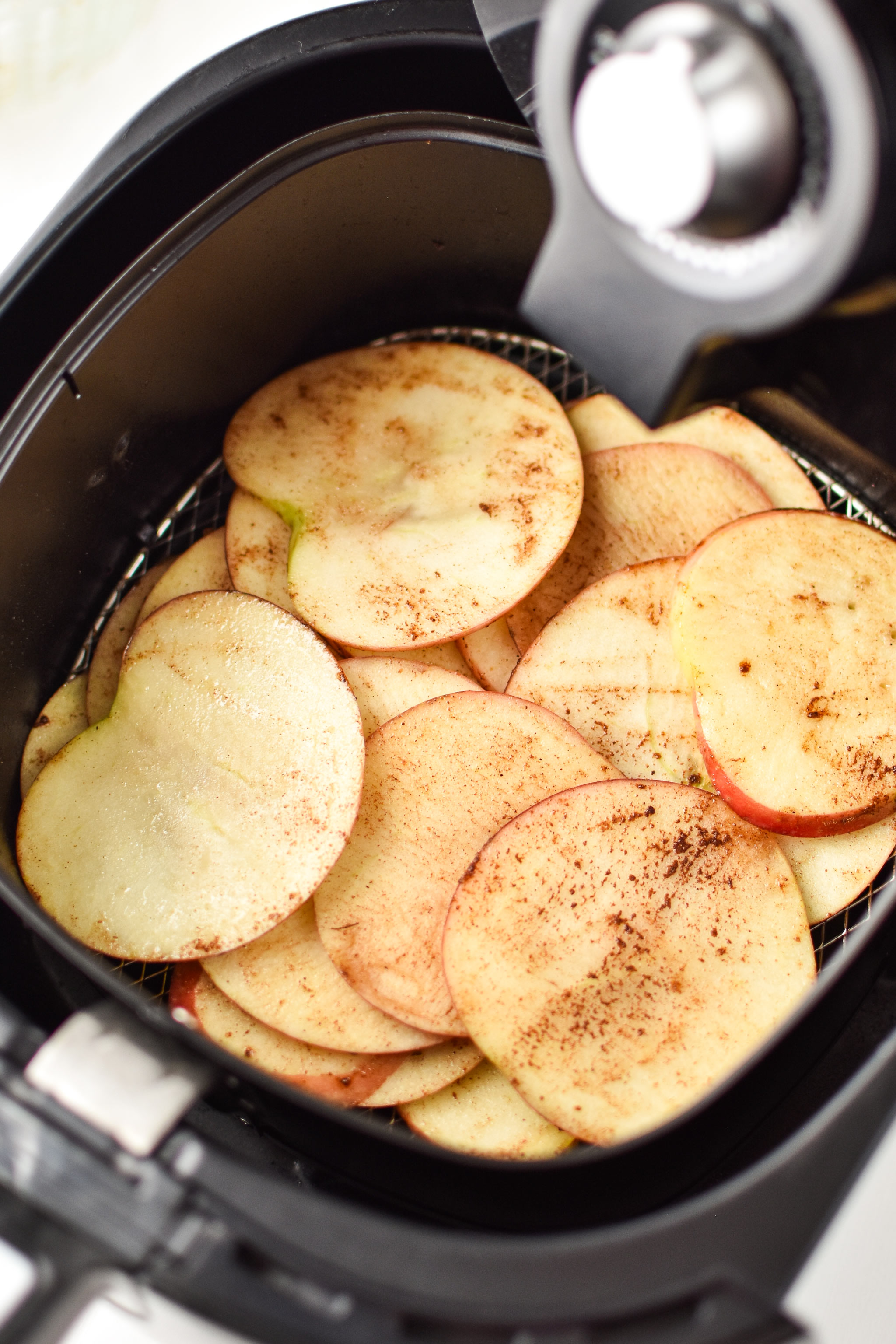 Freshly sliced apples going into the air fryer to make apple chips.