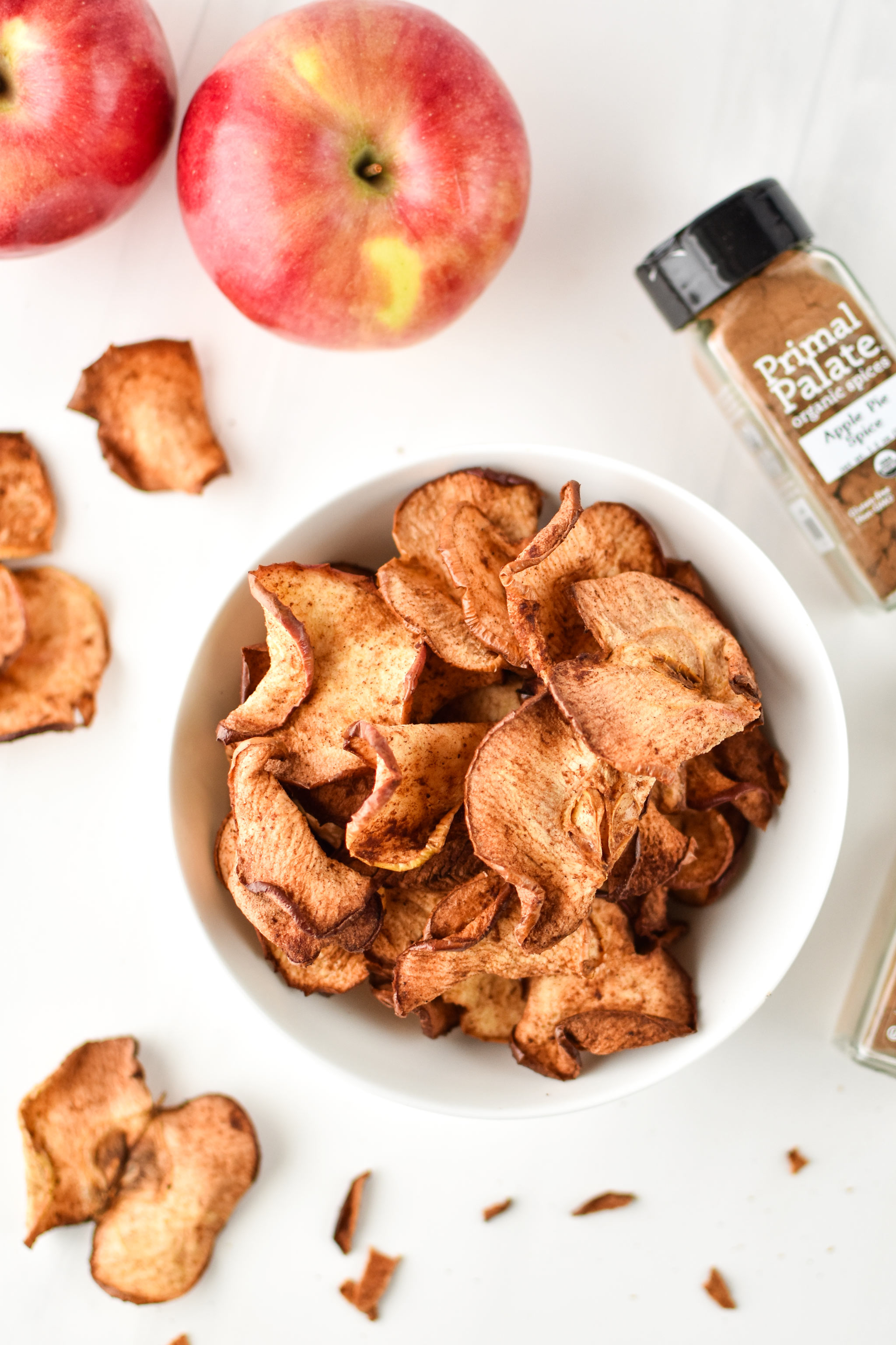 Apple chips photographed from above with apples for how to make apple chips in an air fryer.