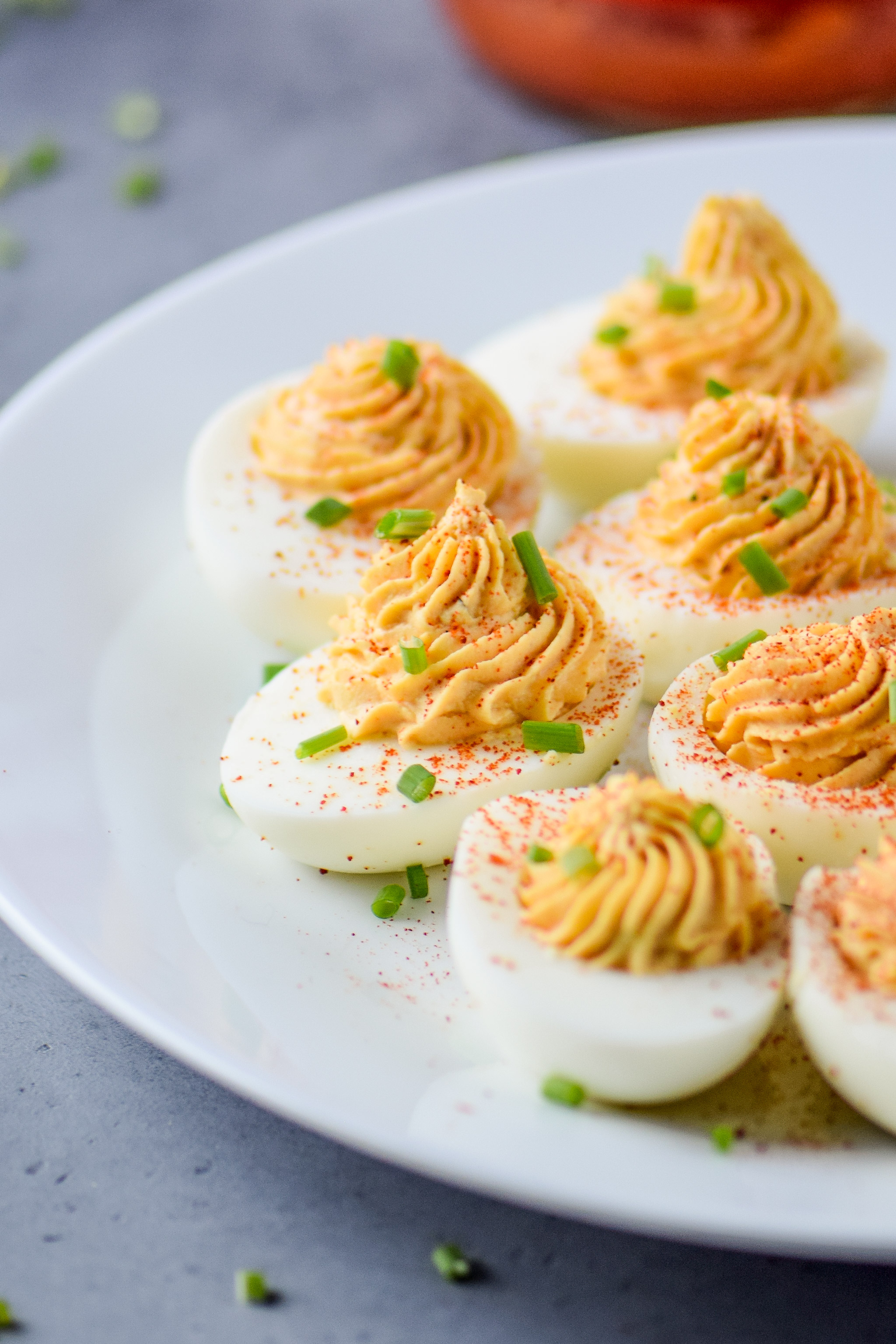 Whole30 Buffalo Deviled Eggs pictured on a plate with smoked paprika and sliced green onions.