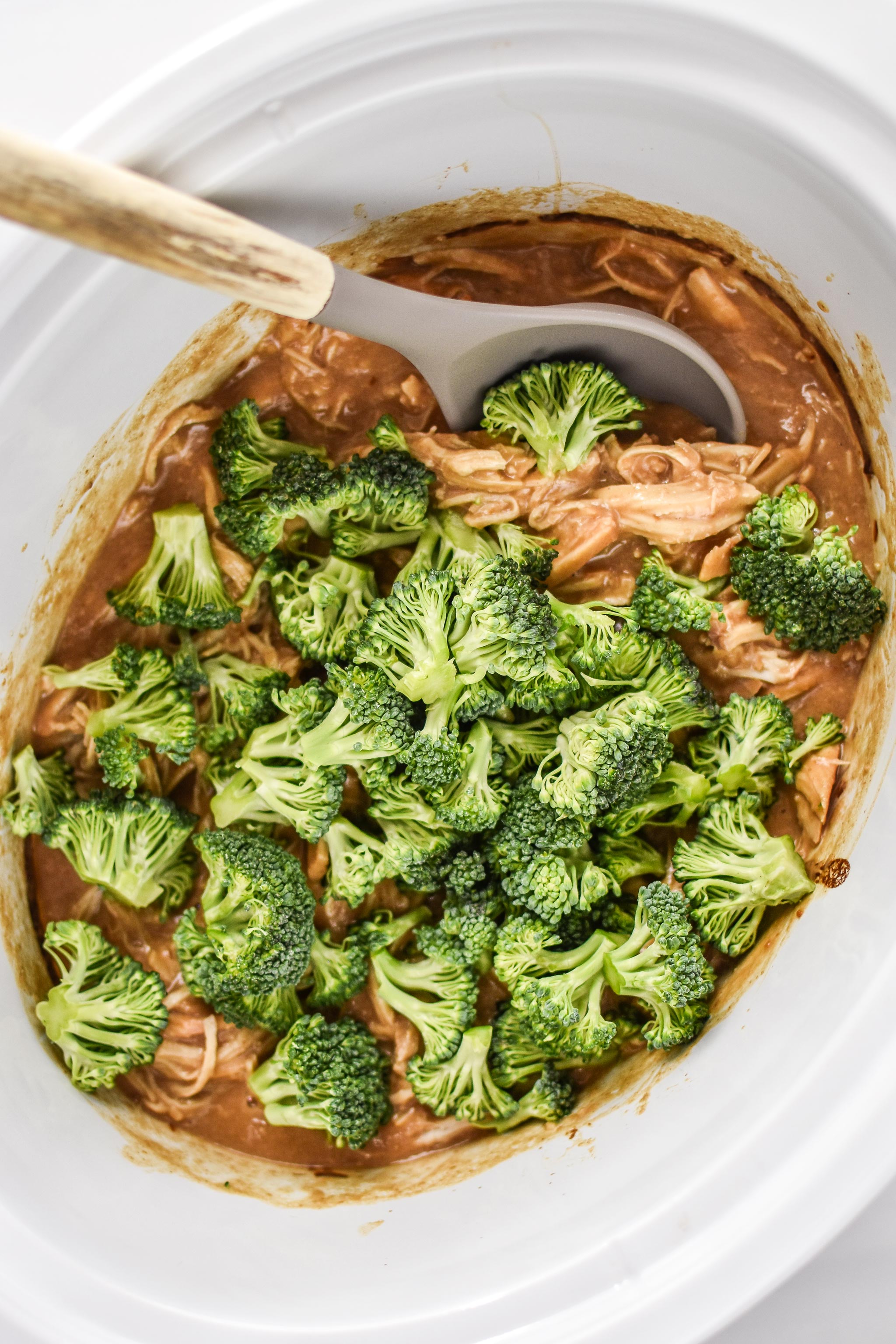 Adding the broccoli florets to the slow cooker after the peanut chicken is cooked 