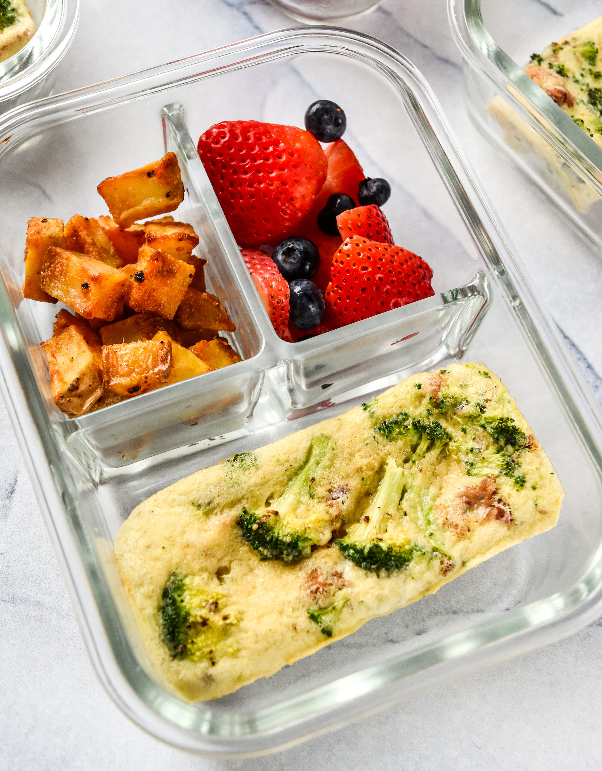 Broccoli bacon mini frittata in a meal prep container with potatoes and berries