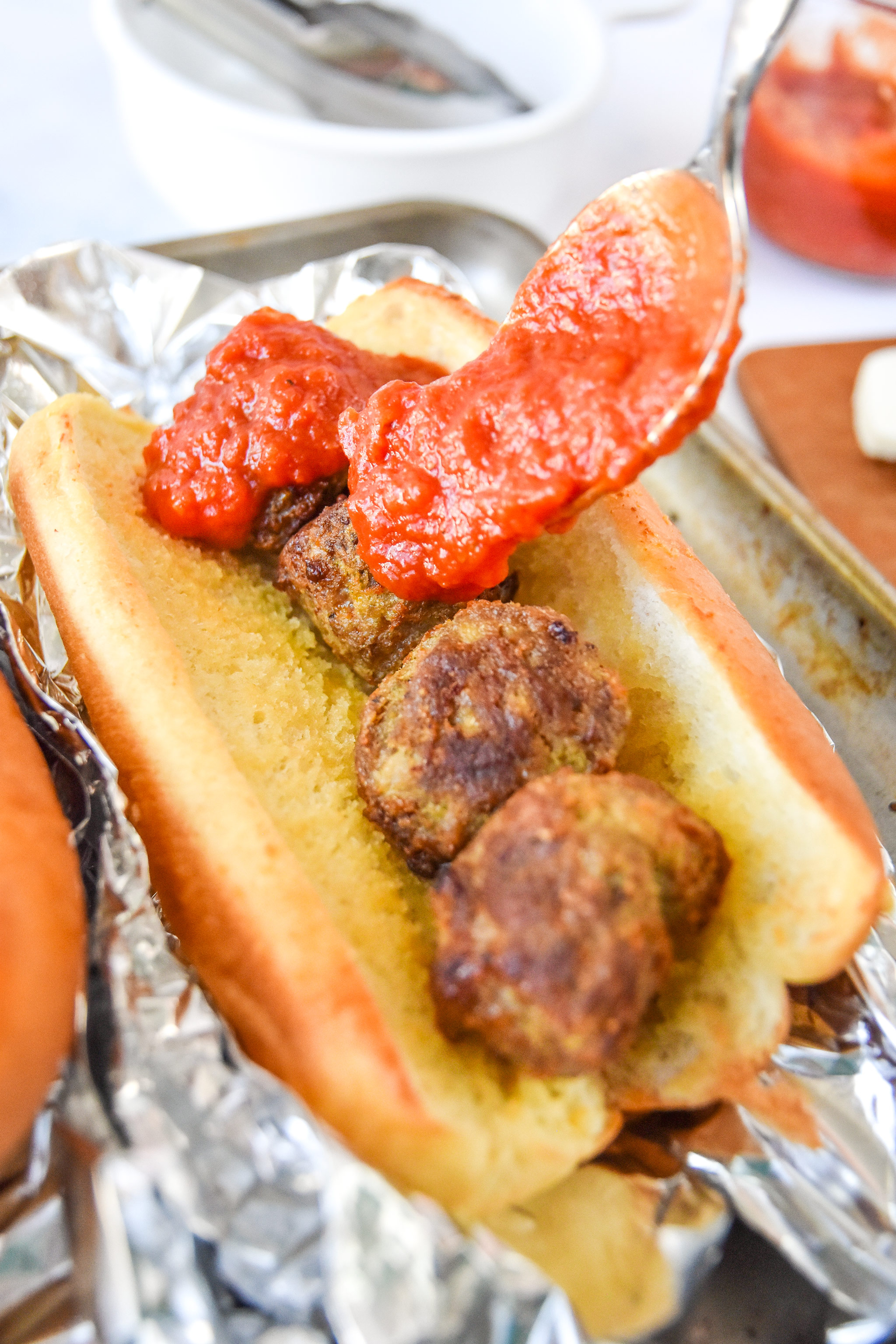 spooning sauce onto the meatballs in the sandwich.