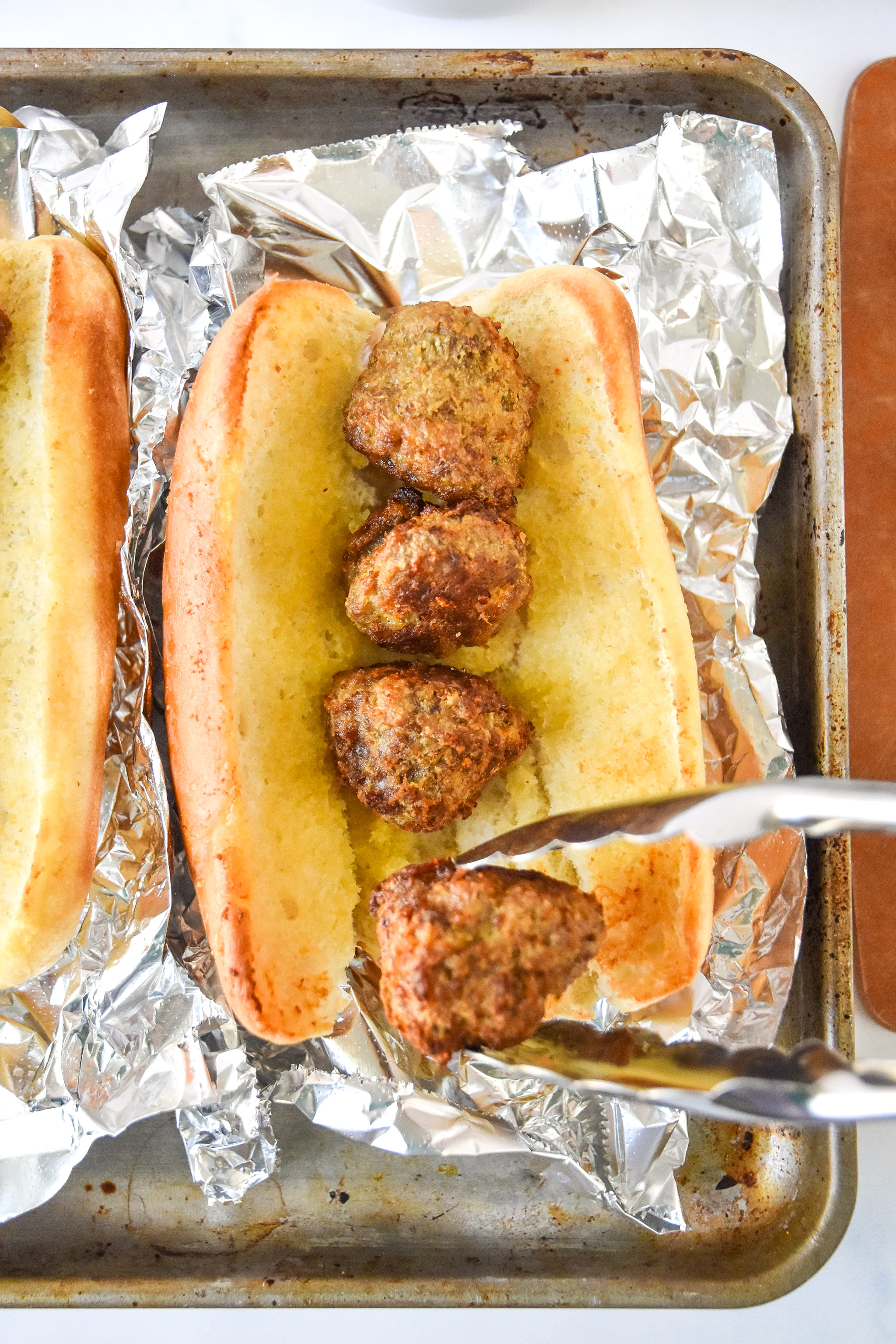 adding meatballs to the hoagie roll with tongs.