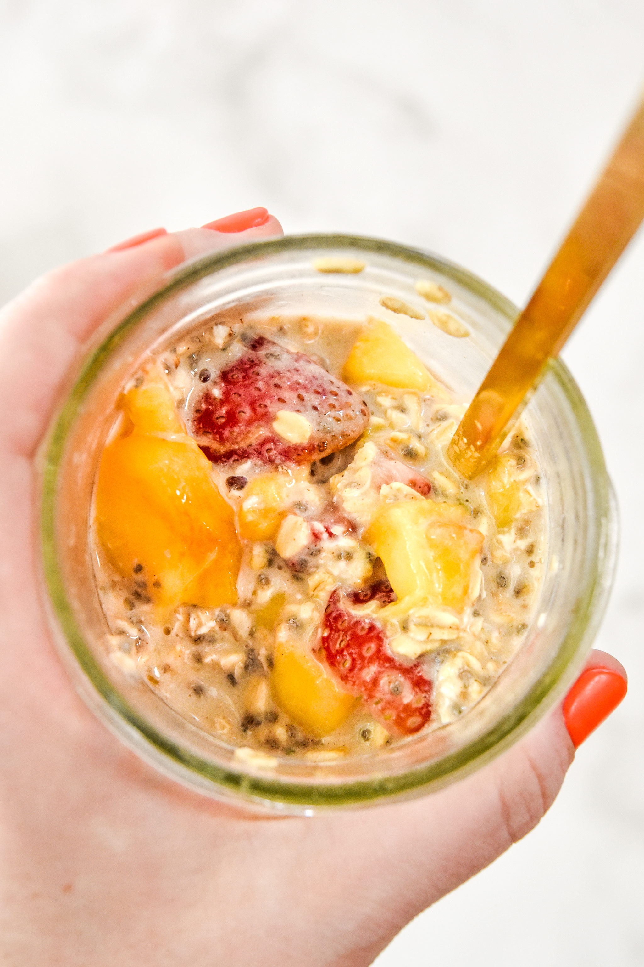 holding a jar of overnight oats with a gold spoon.