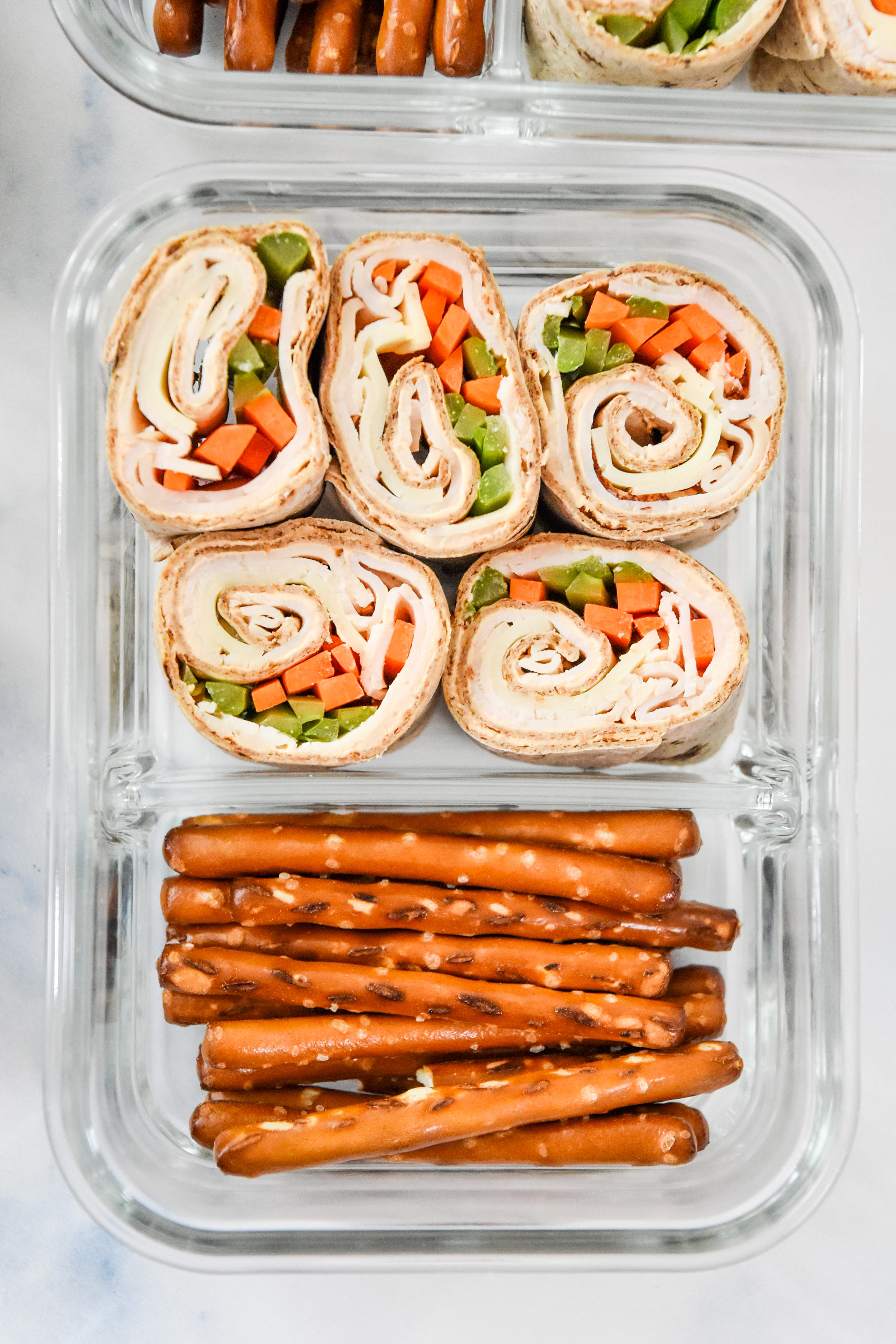 buffalo chicken pinwheels meal prep with pretzels in a glass container.