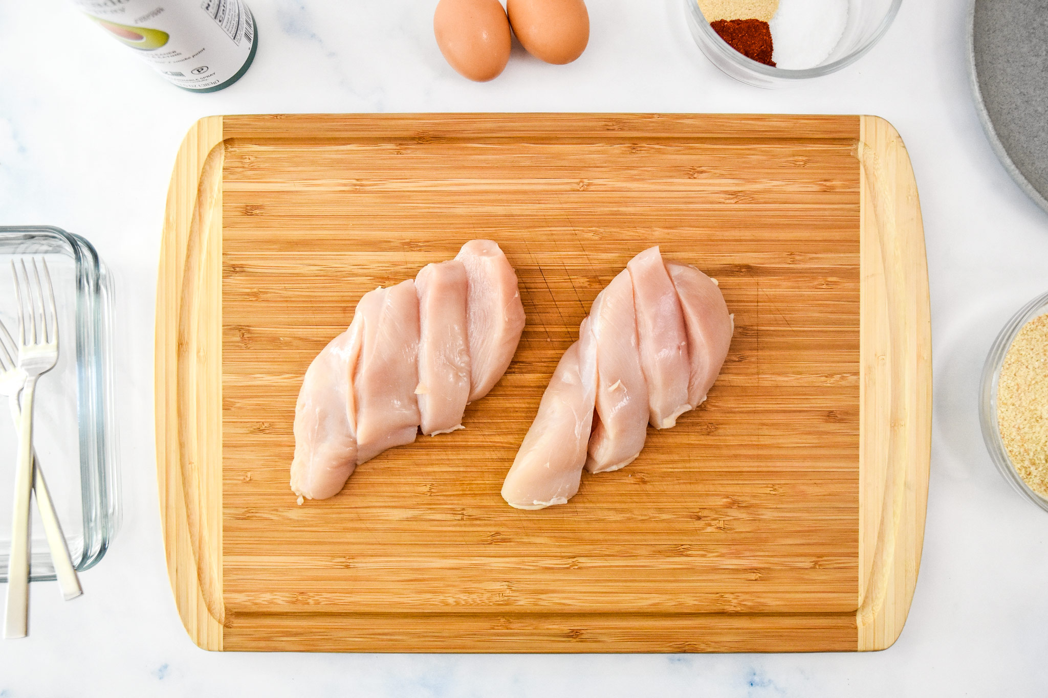 chicken breasts sliced on a cutting board to make chicken tenders.
