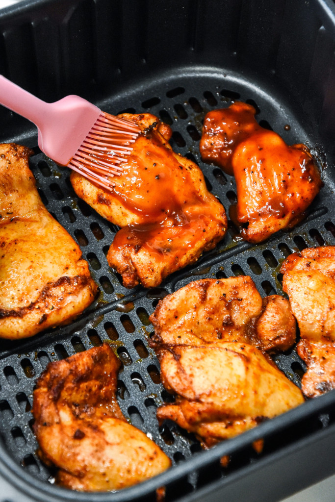 using a pastry brush to add bbq sauce on the chicken thighs.
