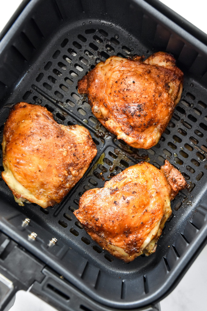 cooked air fryer bone-in crispy chicken thighs in the air fryer basket.
