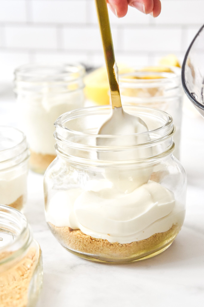 spooning filling into jars to make no-bake cheesecake greek yogurt jars.
