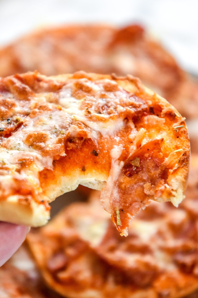 holding a pizza bagel bite with a bite taken out of it.