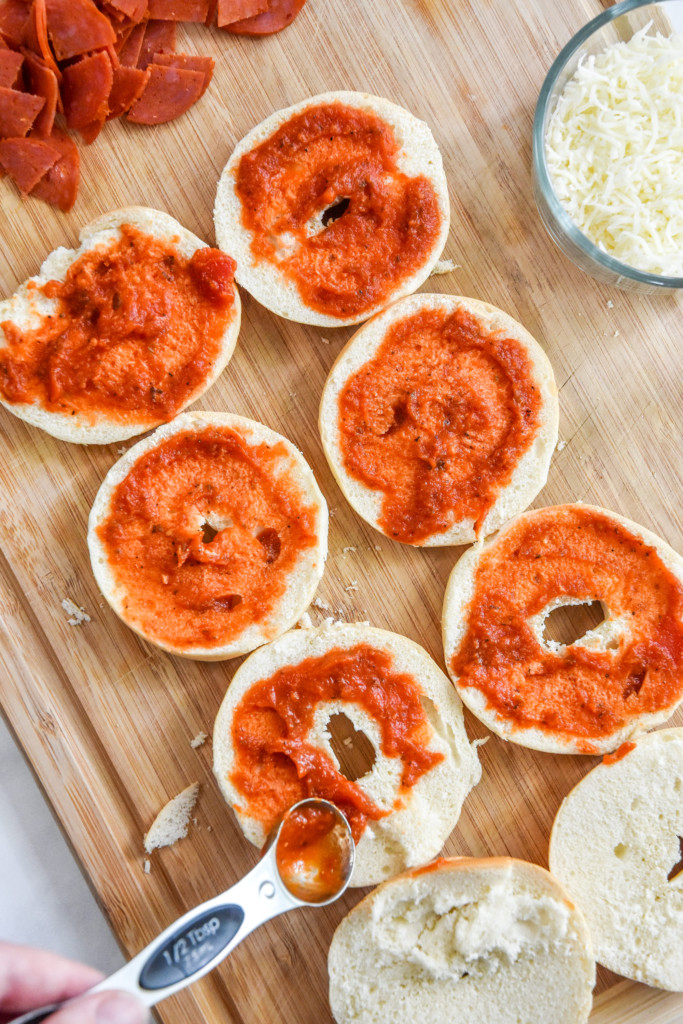 spreading pizza sauce on mini bagels to make air fryer homemade pizza bagel bites.