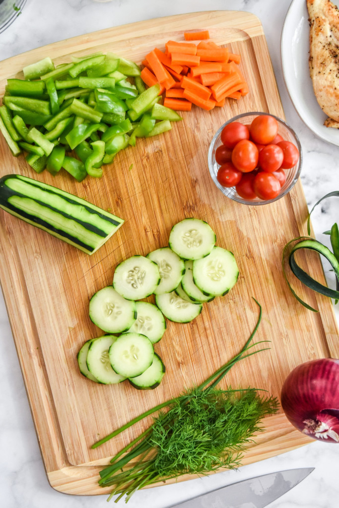 cutting the cucumber and veggies on a cutting board to make chicken bacon ranch salad.