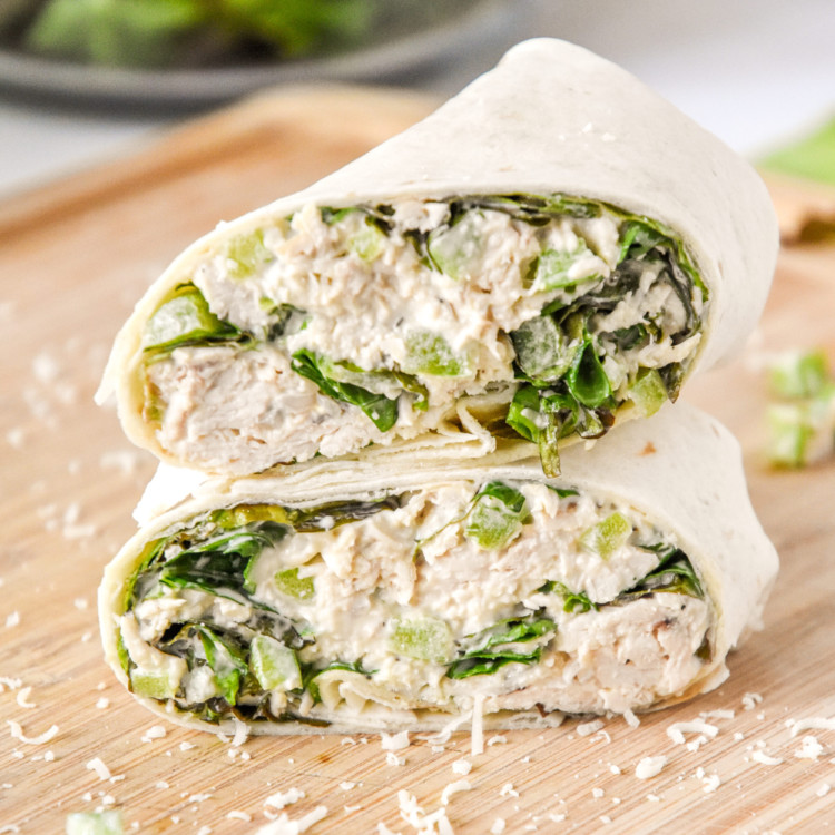 caesar chicken salad lunch wraps cut in half on a cutting board.