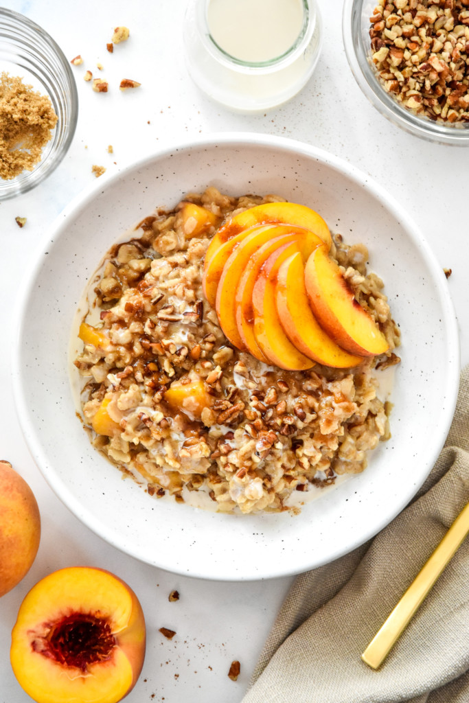 peaches and cream oatmeal in a bowl with fresh peaches and crushed pecans on top.