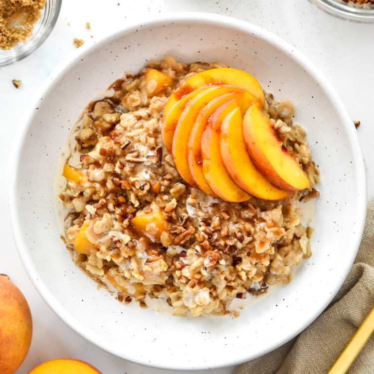 peaches and cream oatmeal in a bowl with fresh peaches and crushed pecans on top.