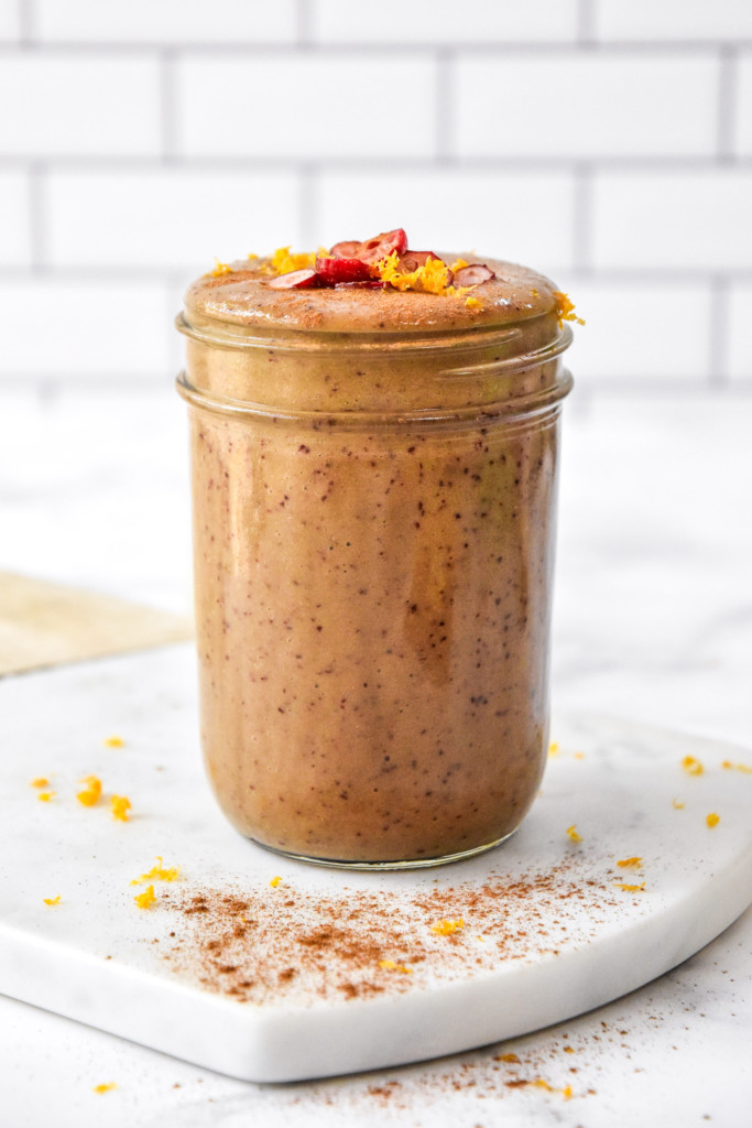 a cranberry orange cinnamon holiday smoothie with sliced cranberries and orange zest on top.