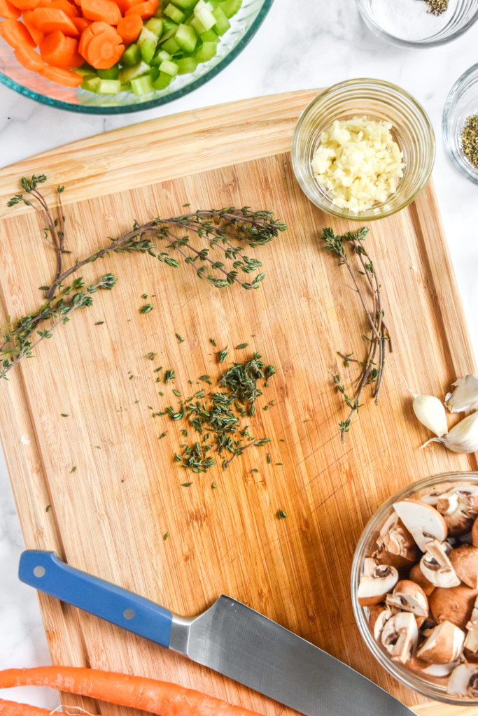 chopping ingredients and thyme on the cutting board for the chicken pot pie with biscuit crust.