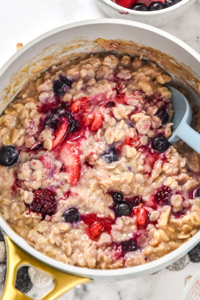 cooked stovetop triple berry egg white oatmeal in a saucepan with spoon.