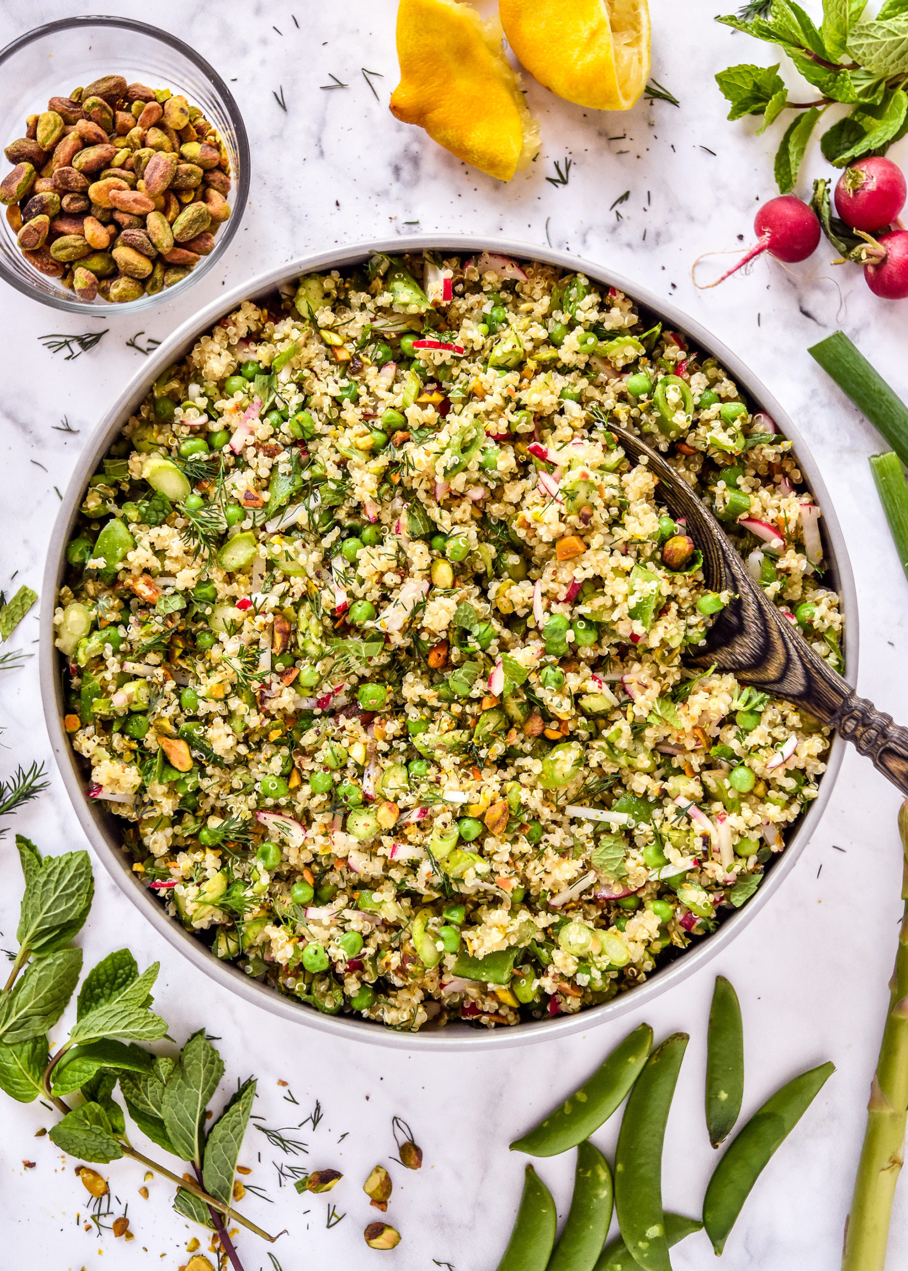 spring vegetable quinoa salad in a serving bowl with wooden spoon.