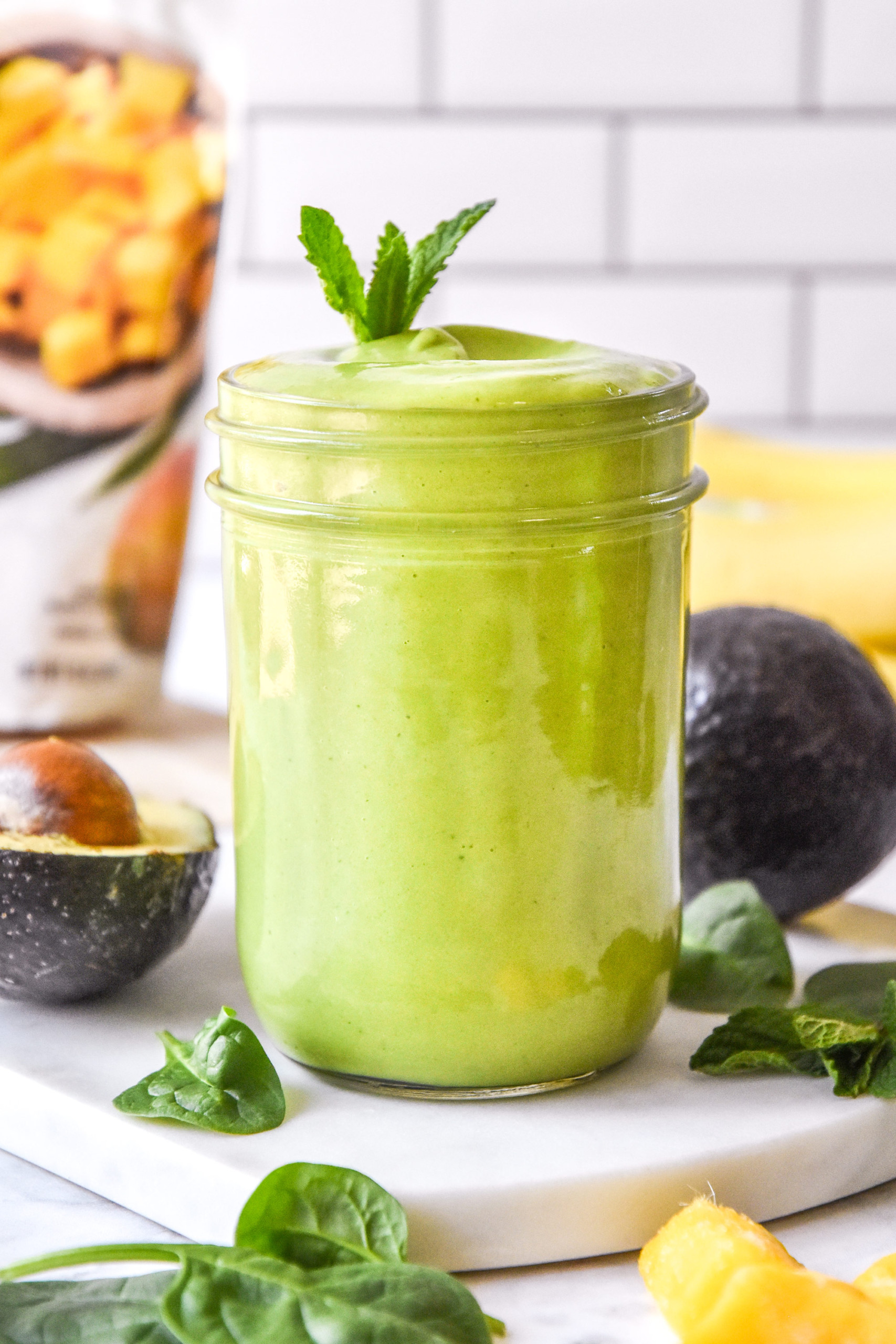 creamy avocado mint green smoothie in a mason jar with a mint leaf on top.