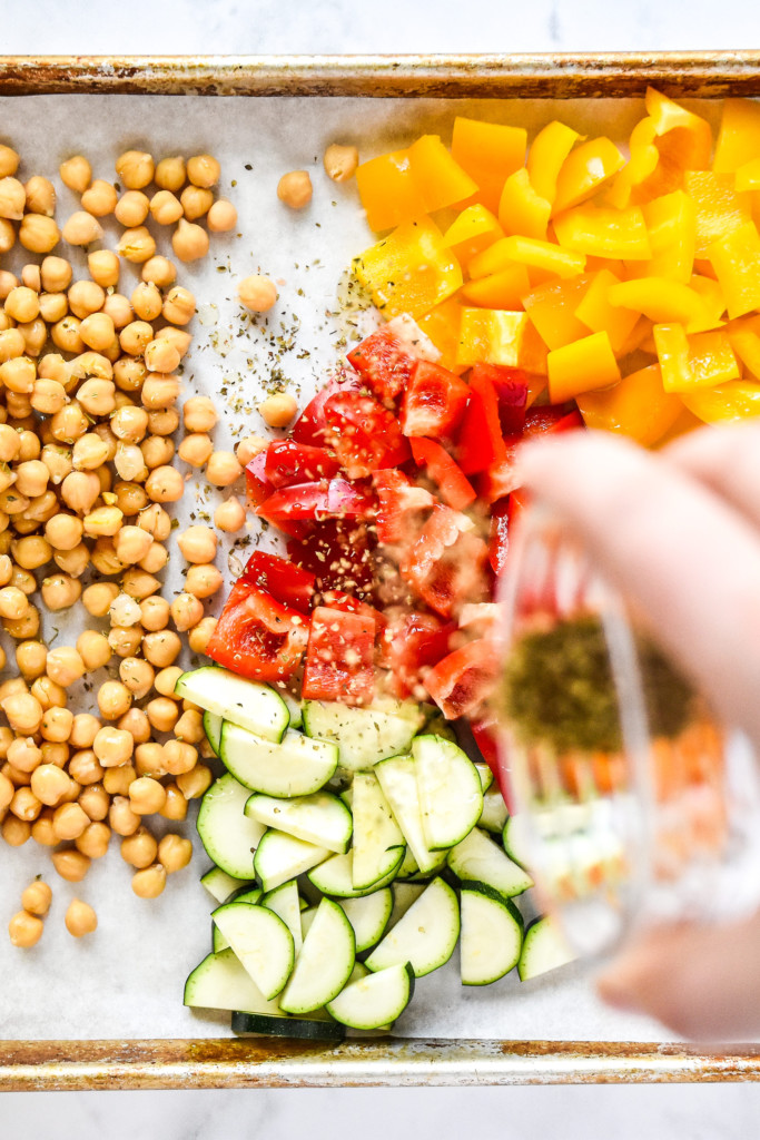 sprinkling oregano on veggies on a sheet pan.