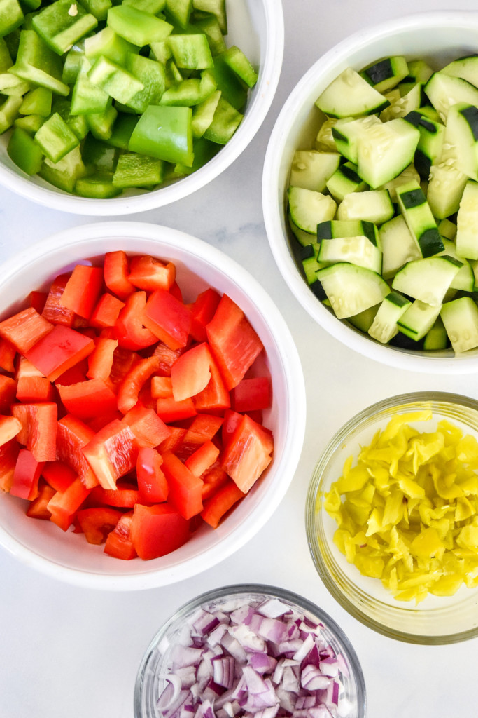 chopped ingredients bell peppers and cucumber in bowls for the pasta salad.