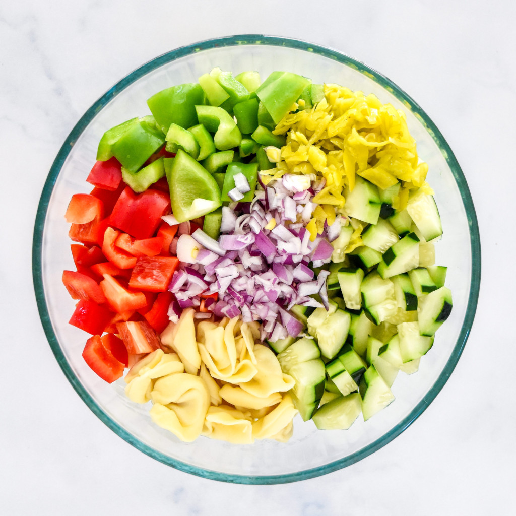 ingredients in a glass mixing bowl before stirring up the zesty italian tortellini pasta salad.