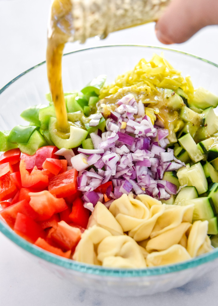 pouring italian dressing into the bowl of ingredients.