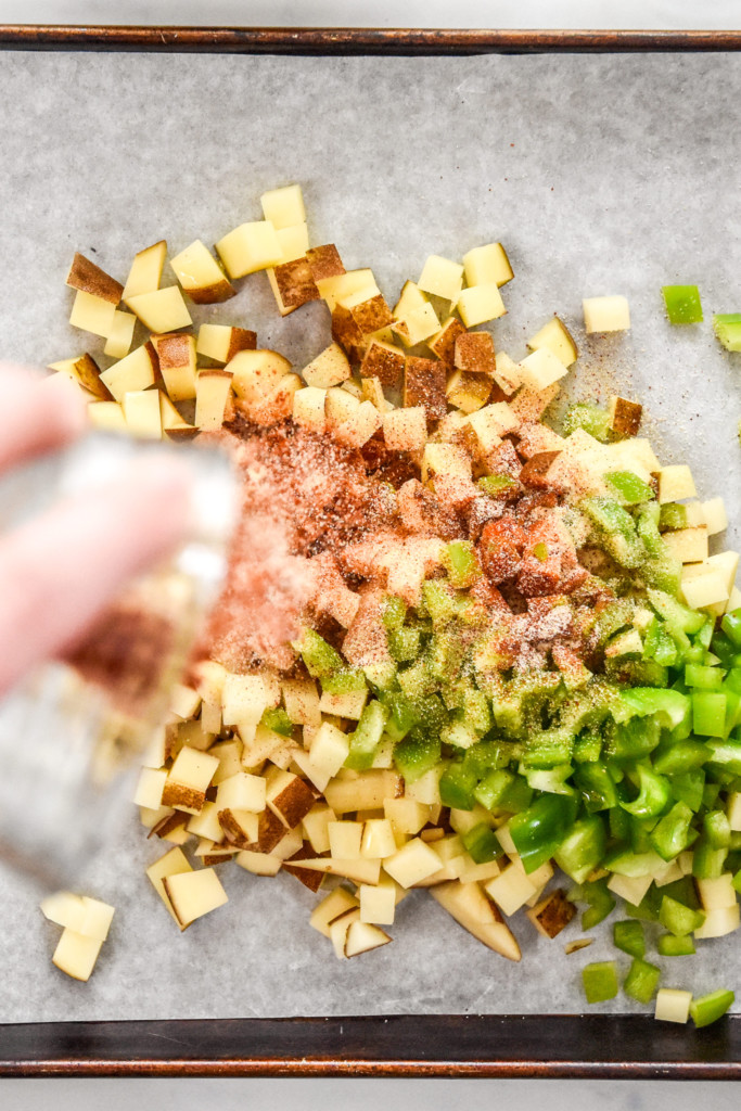 sprinkling spices on diced potatoes on a sheet pan before roasting.