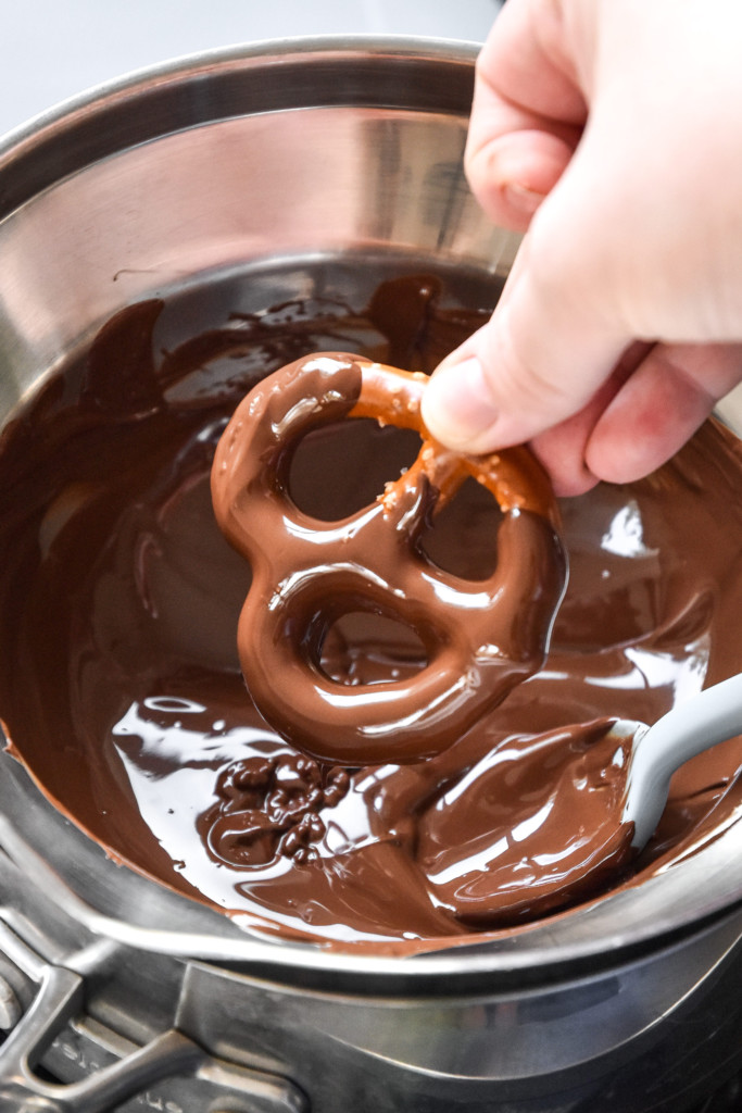 dipping a pretzel in melted chocolate on the stovetop.