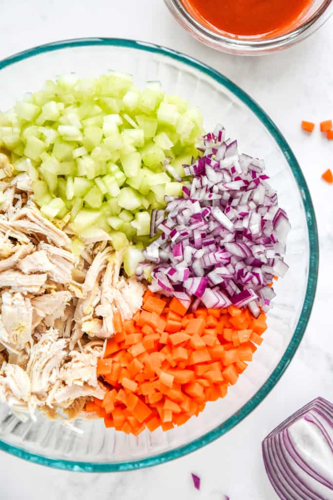 shredded chicken, diced carrots, celery and onion in a glass mixing bowl. 