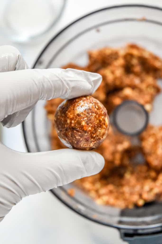 pecan date mixture rolled into a ball held in gloved hands.