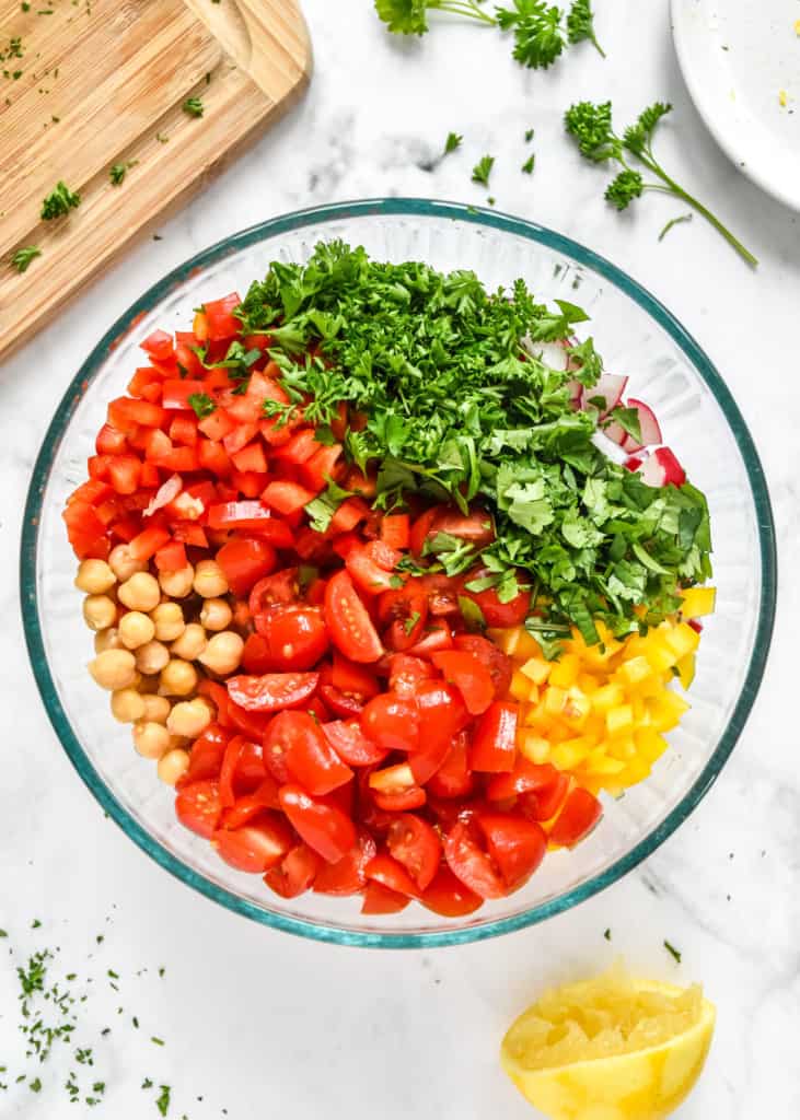 vegetables and chickpeas in a glass bowl before mixing them together.