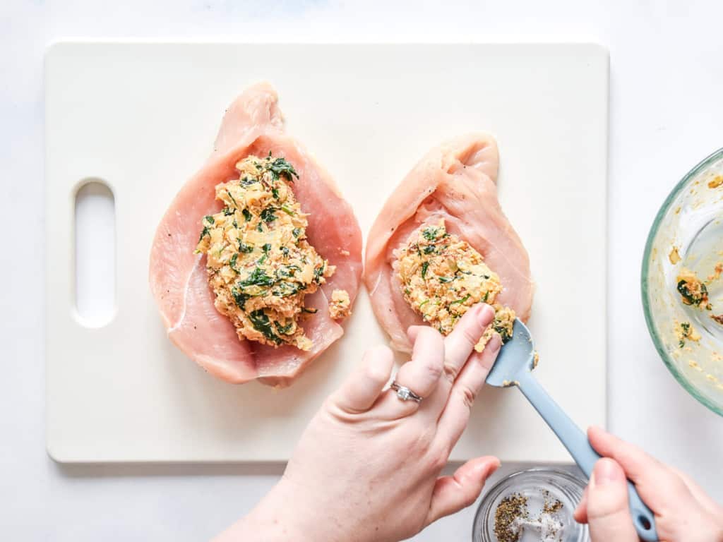 stuffing the cut chicken breasts with cream cheese filling on a white cutting board.
