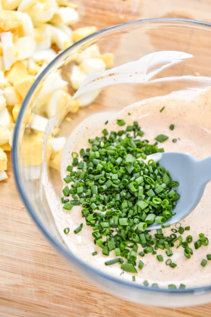 adding chopped chives to the bowl of sauce.