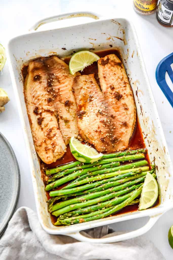fresh from the oven ginger soy tilapia with broiled asparagus in a shallow white baking dish.