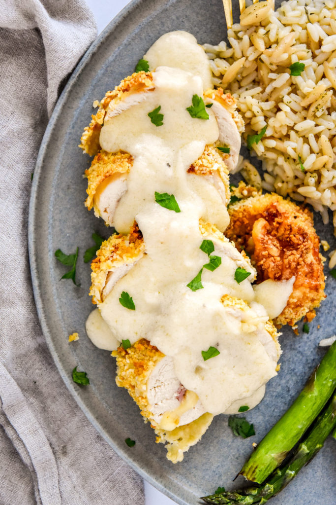 sliced air fryer chicken cordon bleu with creamy cheese sauce on top.