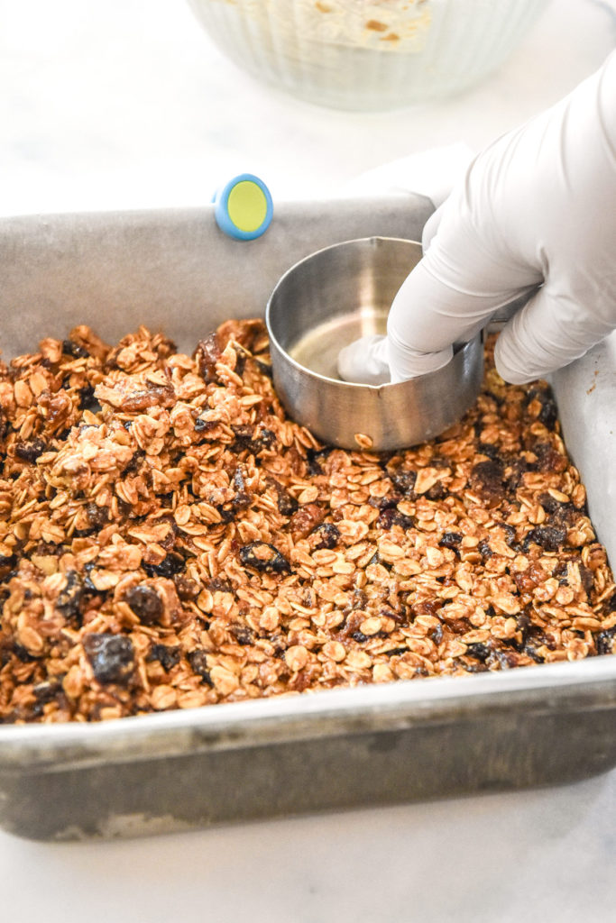 pressing the granola bar mixture into the pan with a measuring cup.