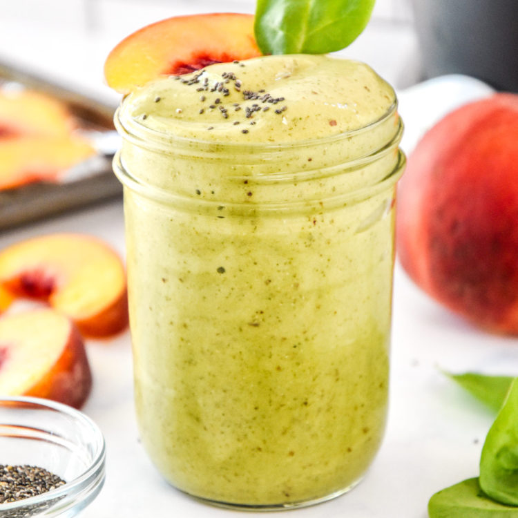 Peaches and green protein smoothie in a glass mason jar with a peach slice on top.