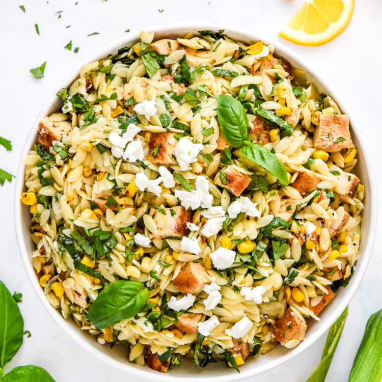 Lemony Chicken & Corn Orzo Salad in a large white bowl with fresh herbs on top.